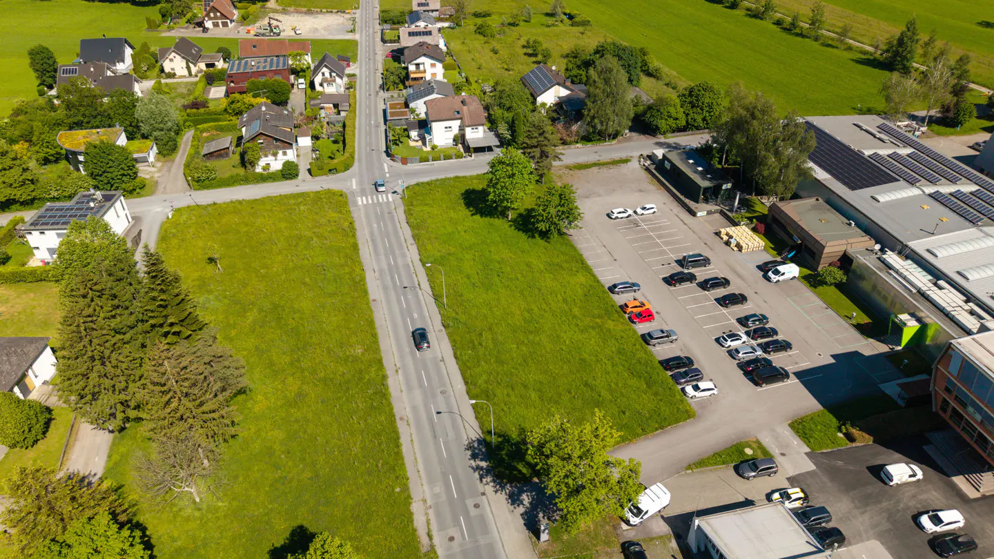 Aerial view of a neighborhood with houses, a road with cars, a green field, and a parking lot next to a building.