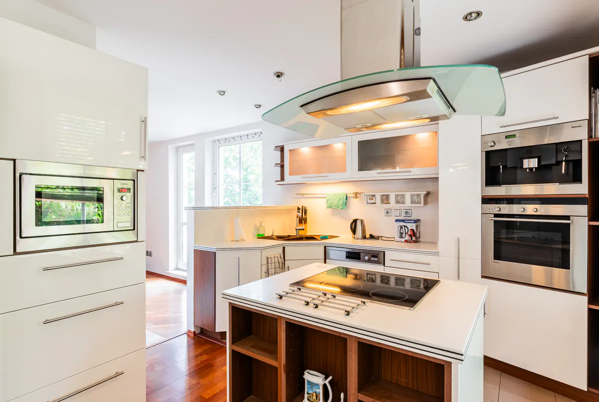 Modern white kitchen with a central island, induction cooktop, stainless steel appliances, and warm wood flooring.