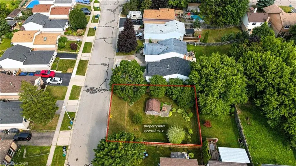 Aerial view of a rectangular property outlined in red, with a small shed, trees, and surrounding houses.