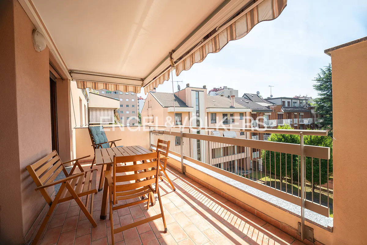 Balcony with a table and chairs, awning, and view of buildings and trees.