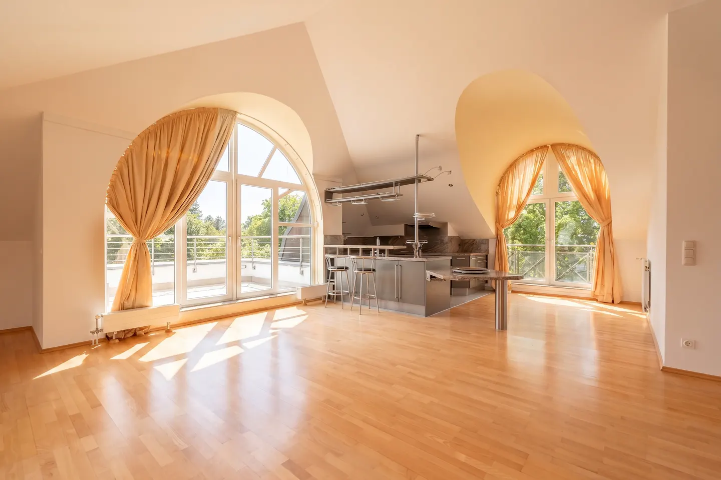 Bright, open apartment with wood floors, arched windows with gold curtains, and a stainless steel kitchen island with bar stools.