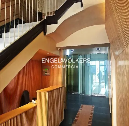 Office lobby with wood paneling, a reception desk, and glass doors leading outside. Stairs are visible on the left.