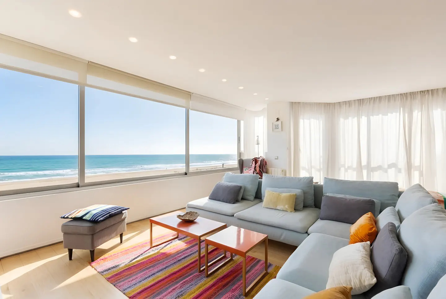 Bright living room with a large blue sectional sofa, colorful rug, and ocean view through large windows.