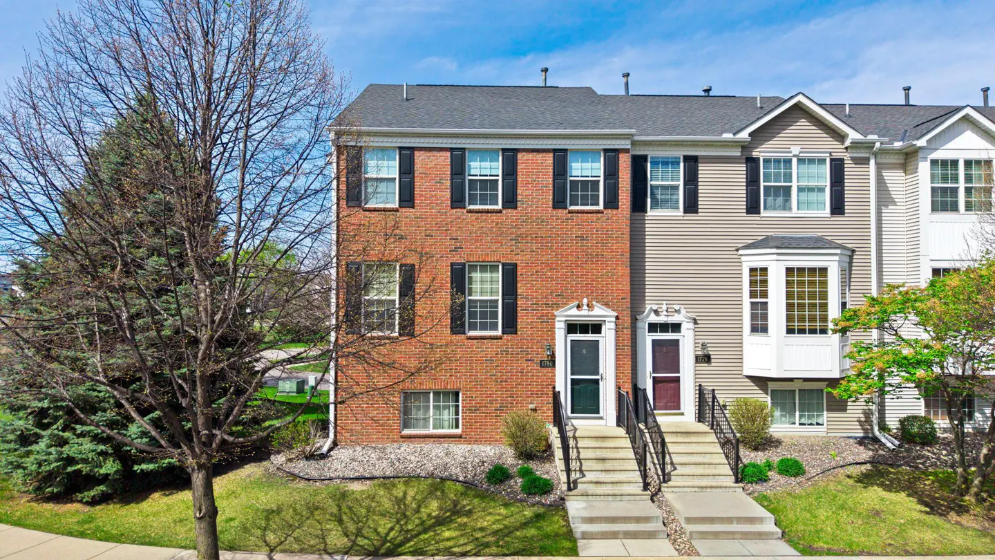 Exterior view of a brick and siding townhouse with black shutters, a gray roof, and a small front yard.