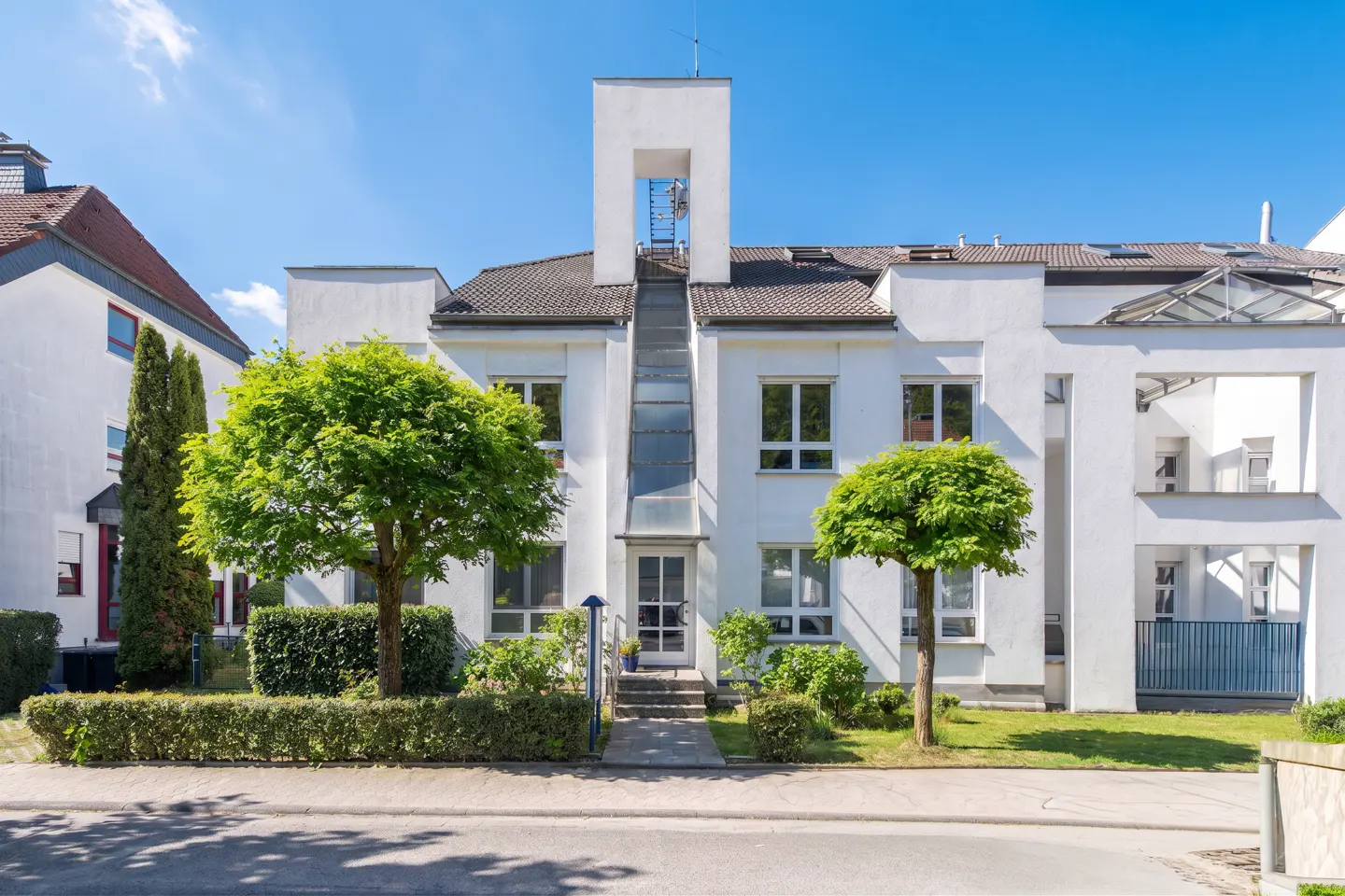 Exterior of a modern white apartment building with green trees and blue sky.