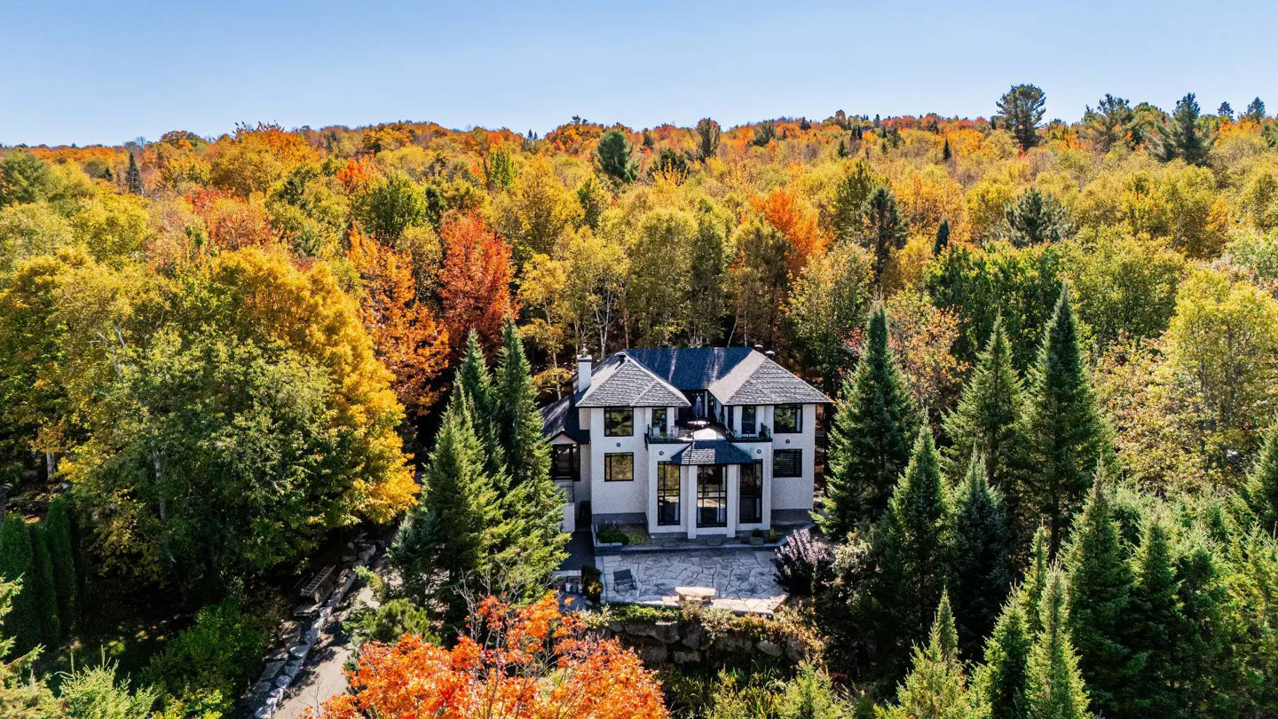 Two-story white house with a gray roof surrounded by colorful autumn trees under a blue sky.