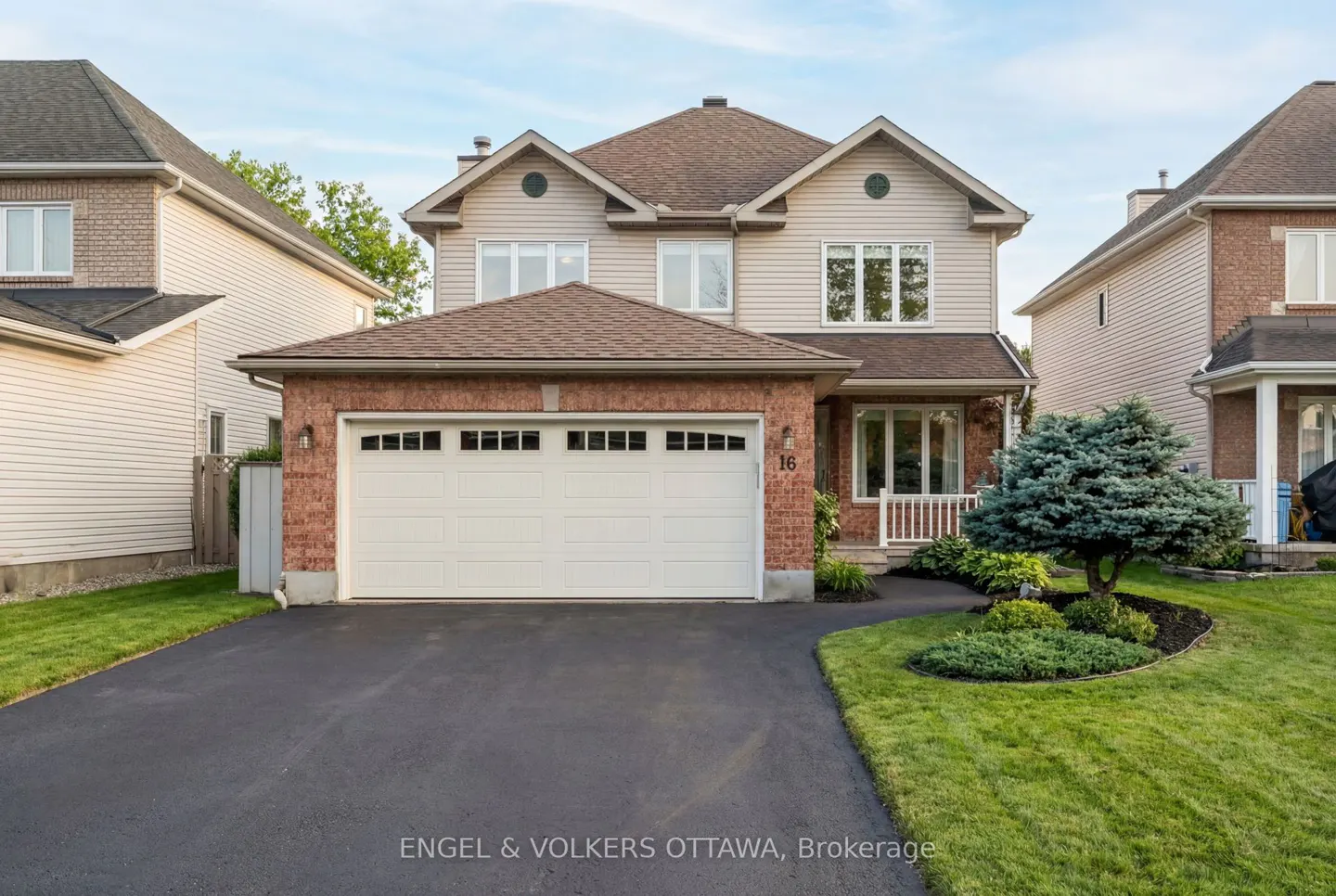 Two-story house with beige siding, a brick garage, and a dark asphalt driveway. A manicured lawn and landscaping add curb appeal.
