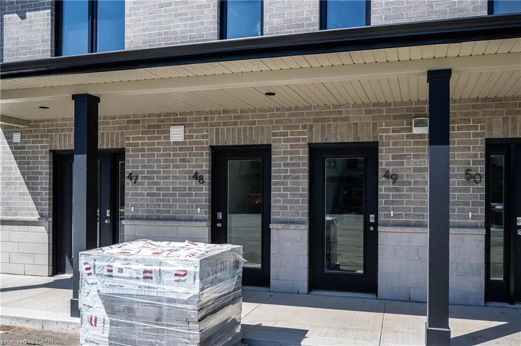 Exterior view of a light brick apartment building with black doors numbered 47-50. A wrapped pallet sits on the concrete porch.