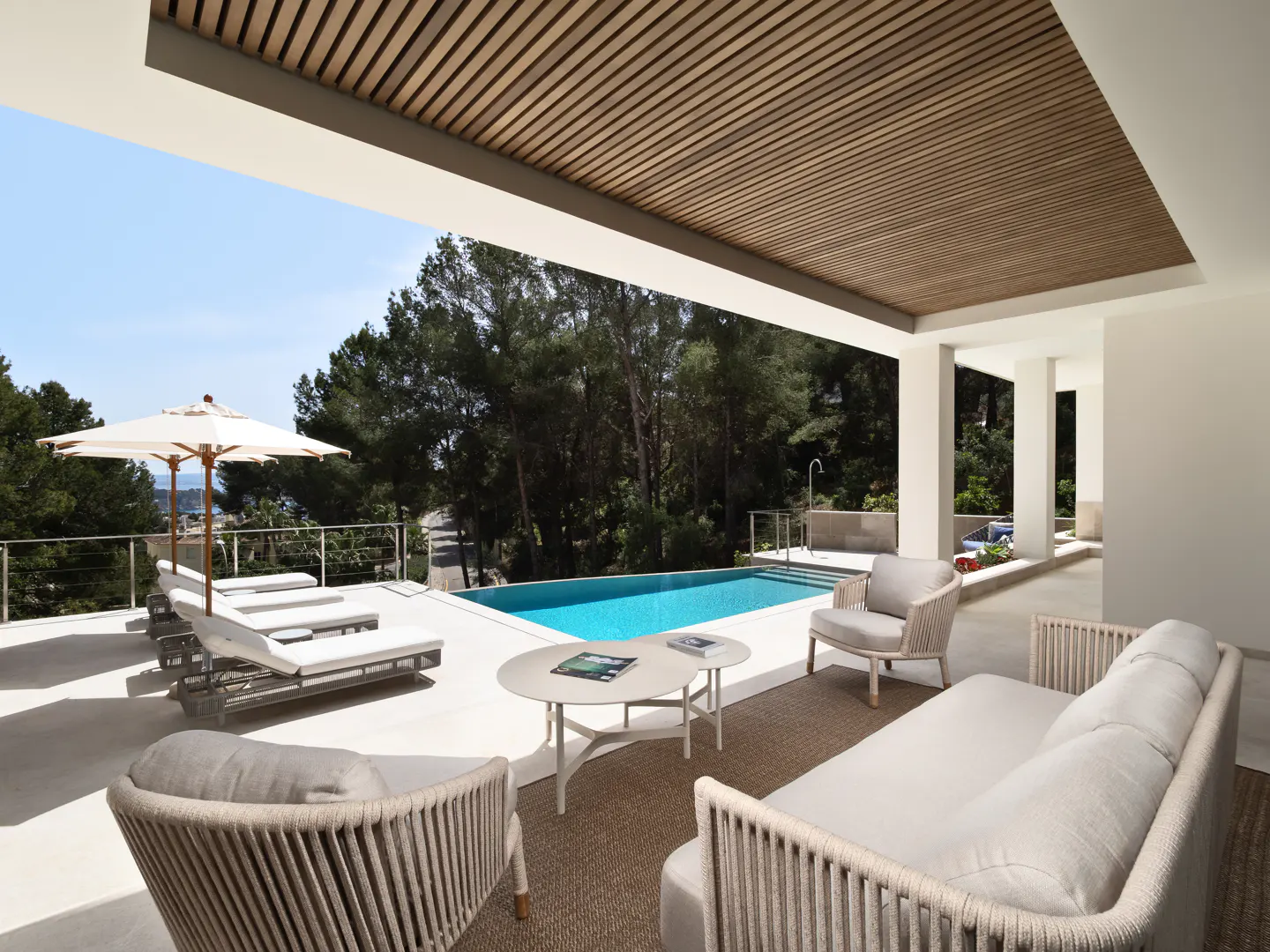 Luxury patio with a pool, lounge chairs, and seating area. Trees and blue sky are visible in the background.