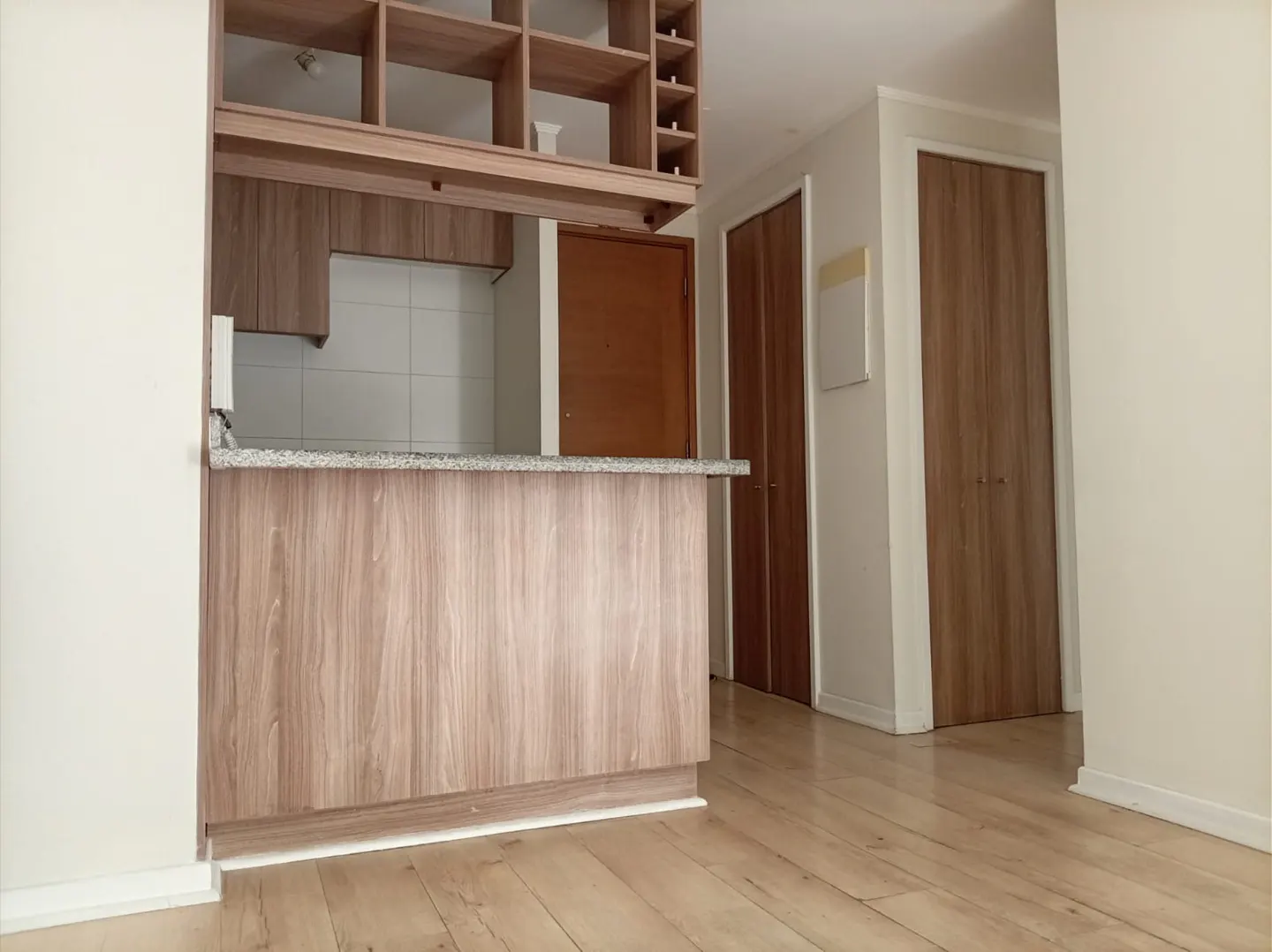 Interior view of a kitchen with wood cabinets, a granite countertop, and a wooden floor. Two wooden doors are visible in the background.