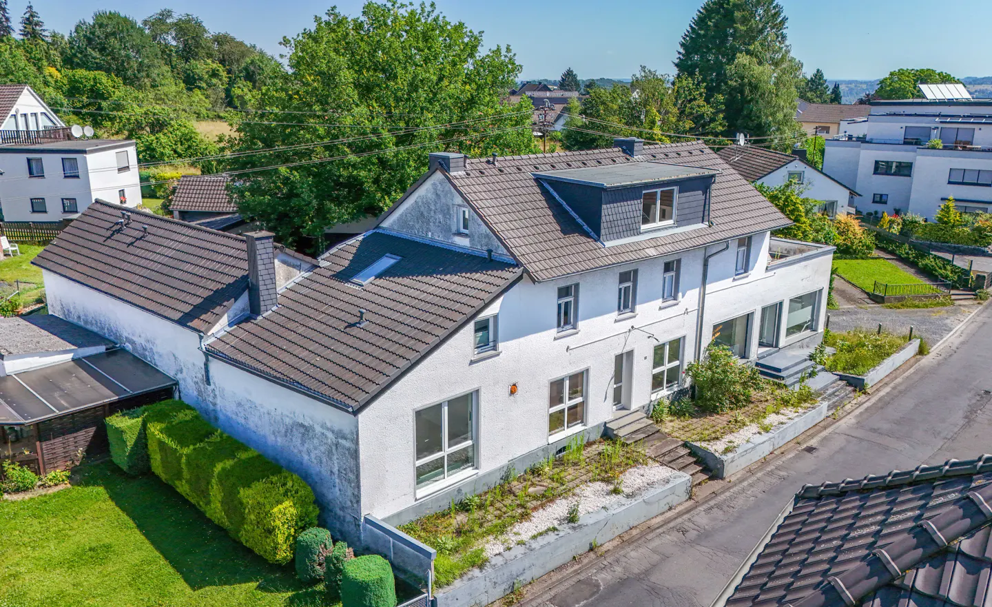 Aerial view of a two-story white house with a gray tiled roof, surrounded by green trees and lawns.
