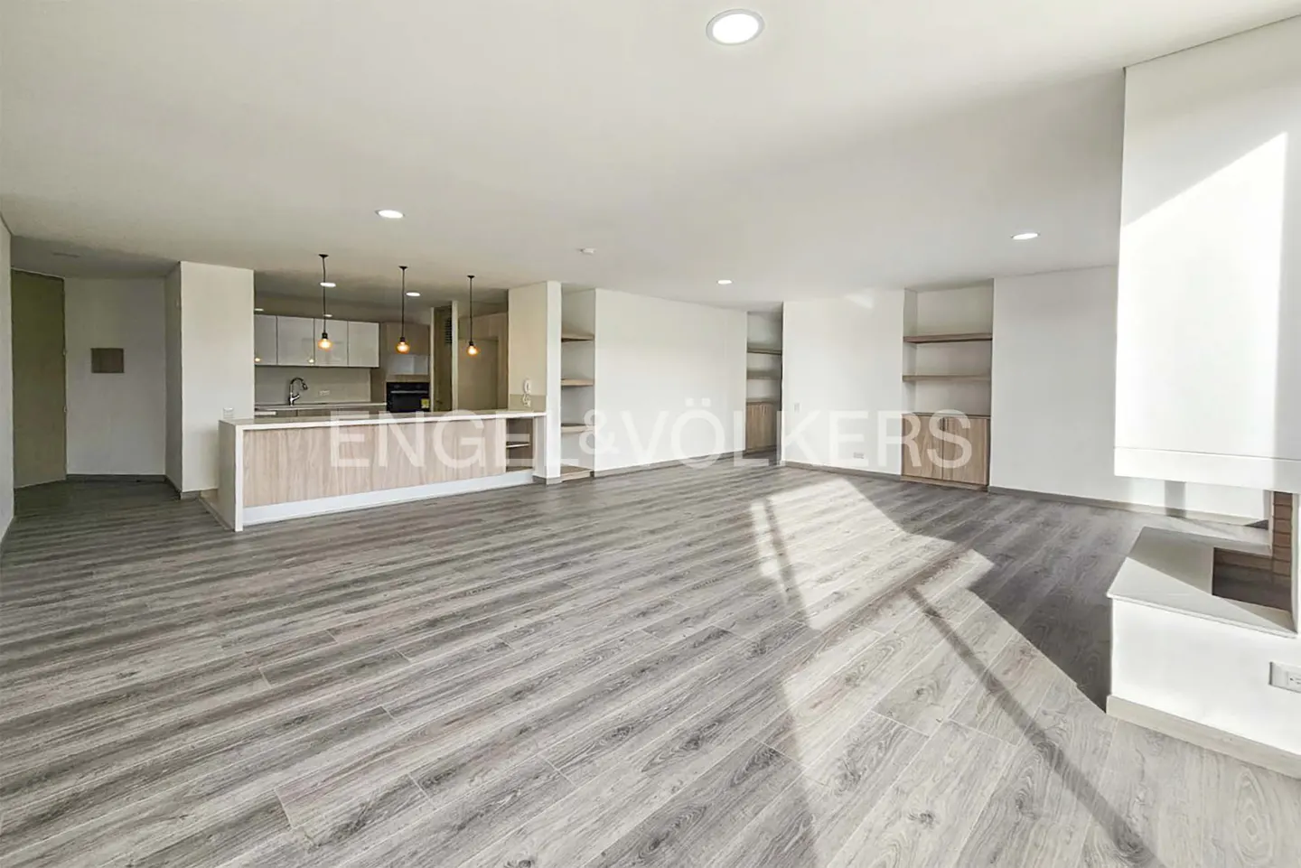 Spacious open-plan living area with light wood-look flooring, a modern kitchen island, and built-in shelving.