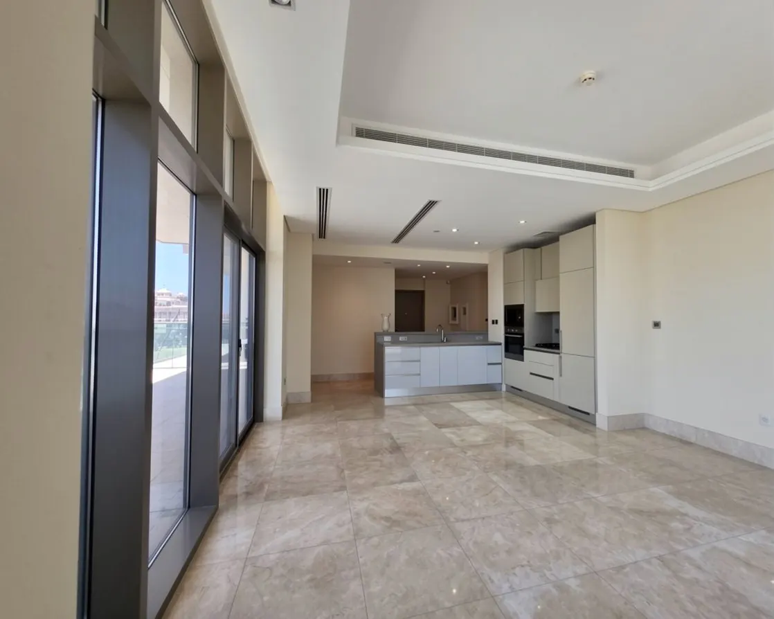 Modern open-plan kitchen with light grey cabinets, marble floors, and floor-to-ceiling windows overlooking a balcony.