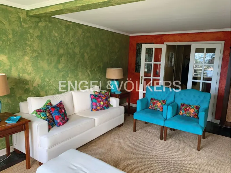 Living room with white sofa, turquoise chairs, and colorful pillows. Walls are green and orange. French doors lead to another room.