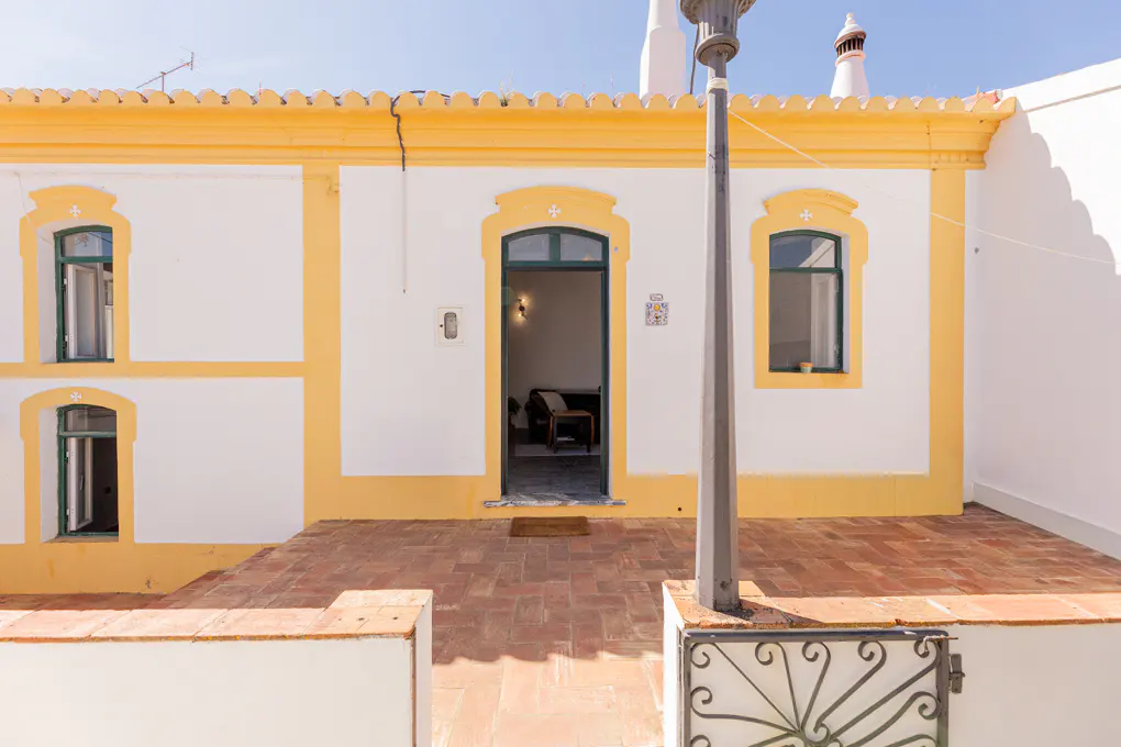 Exterior view of a white house with yellow trim, green windows and door, and a brick patio.