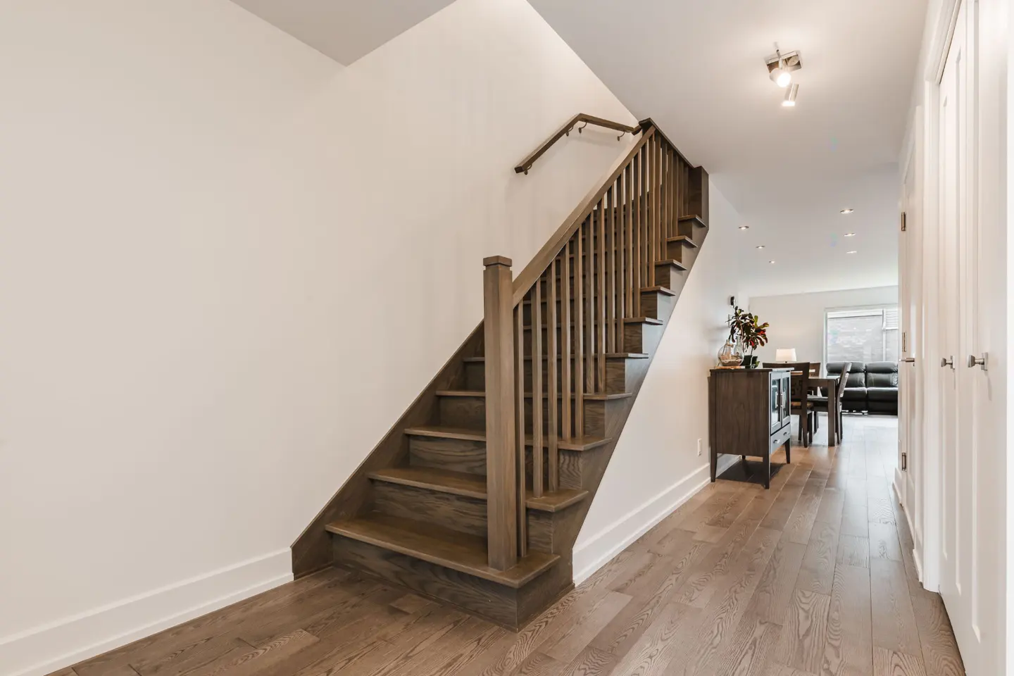 Interior view of a home featuring a wooden staircase with white walls and hardwood floors. A glimpse of the dining area is visible.