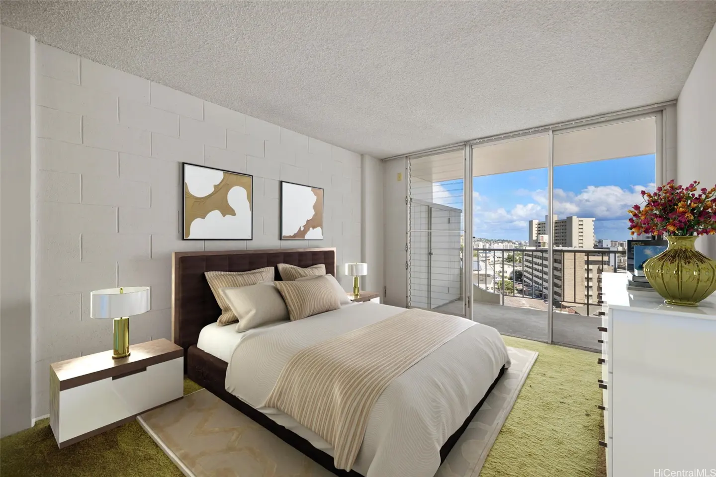 A bright bedroom with a brown bed, white linens, and a city view from the balcony. Two framed art pieces hang above the bed.