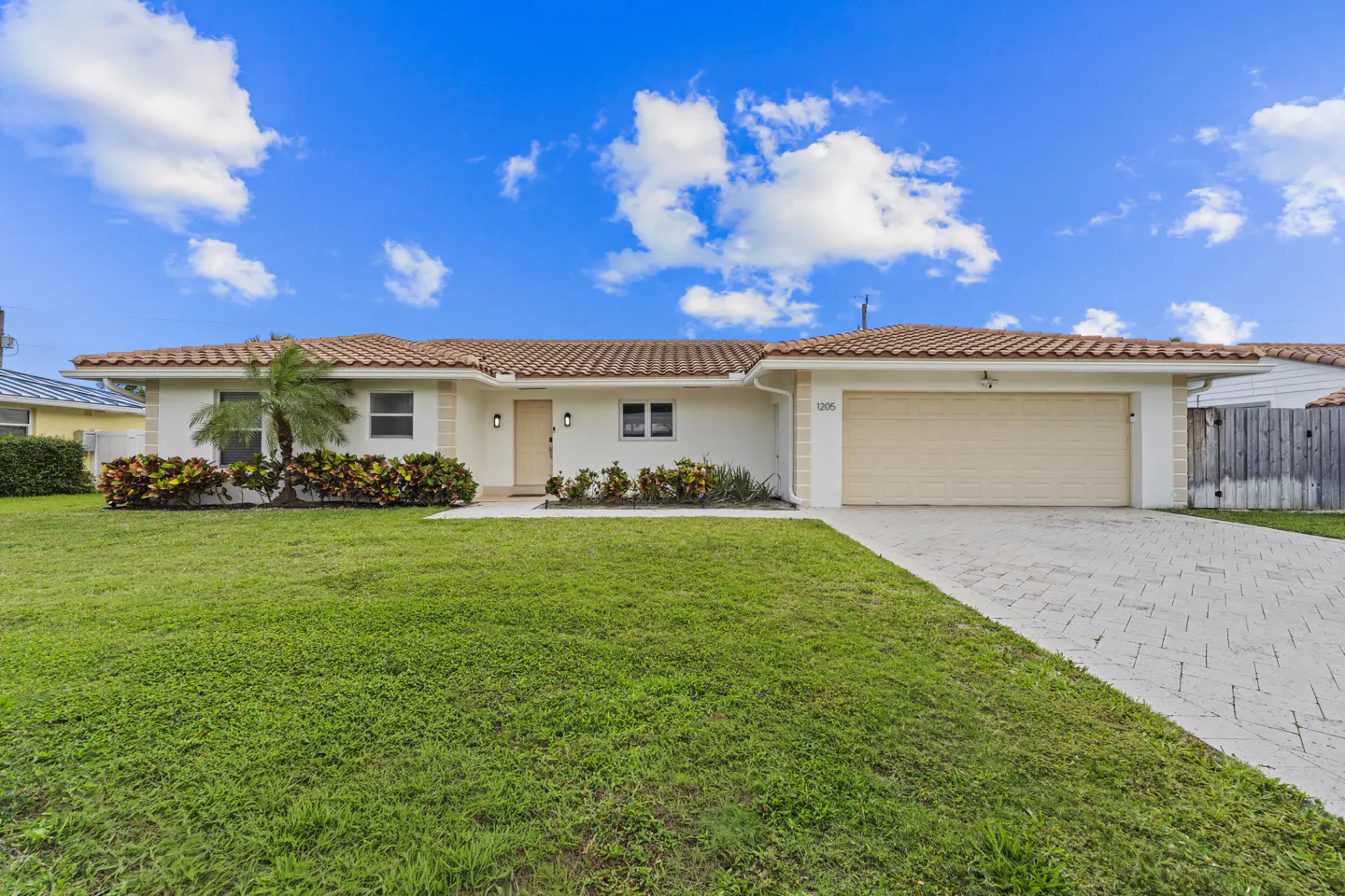 A single-story home with a red tile roof, white exterior, and a green lawn under a blue sky.