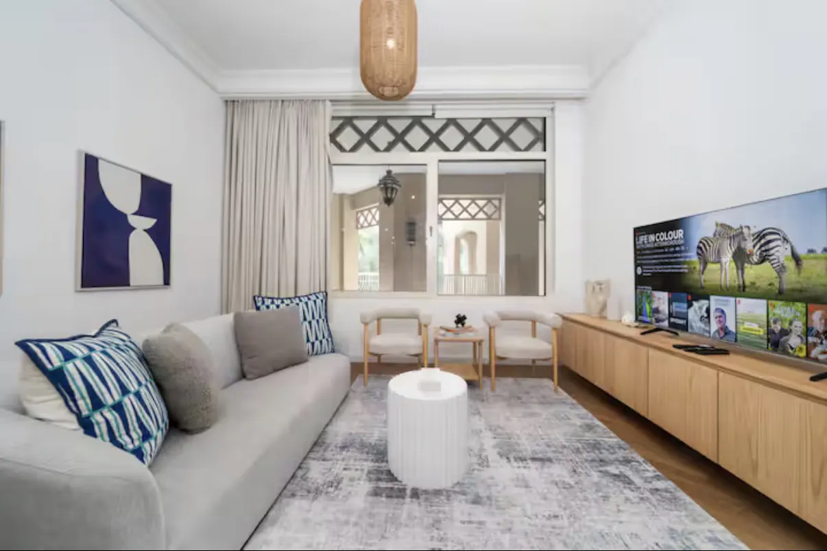 Living room with a gray sofa, blue pillows, a white table, and a TV showing zebras.