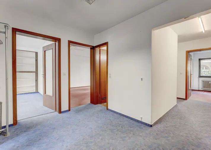 Empty hallway with blue patterned carpet, white walls, and multiple wooden door frames leading to adjacent rooms.