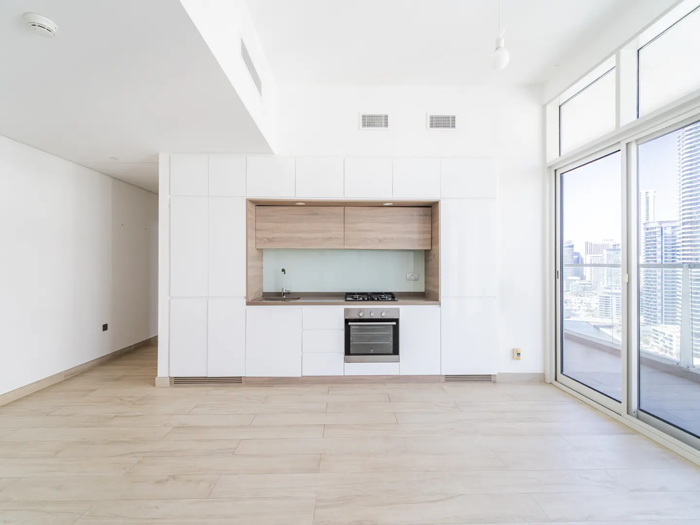 Bright, modern apartment with white cabinets, stainless steel appliances, and a city view from the sliding glass doors.