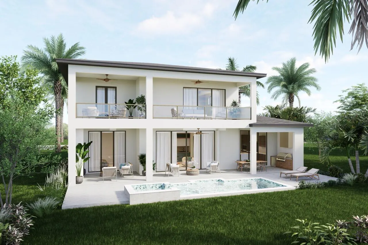 Two-story white house with balconies, a pool, and outdoor seating surrounded by green grass and palm trees.