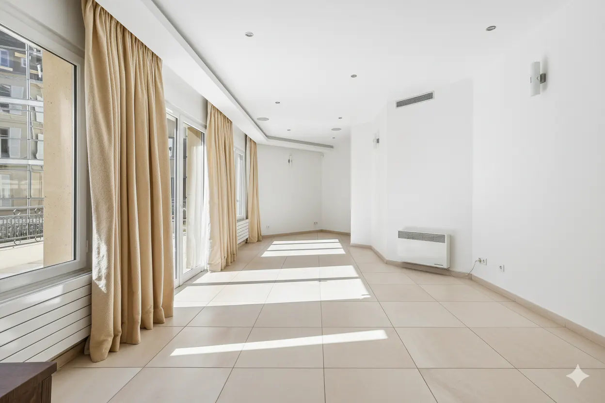 Bright, empty room with beige tile floor, white walls, and tall windows with beige curtains. Sunlight streams in.