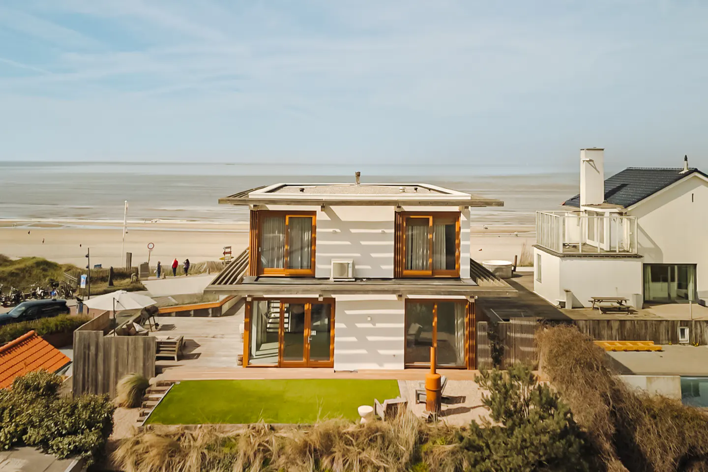 Two-story white house with wood trim near a beach. The house has a flat roof and large windows.