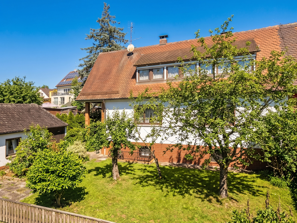 A white house with a brown tiled roof and a green garden with trees under a clear blue sky. [AI-generated text]