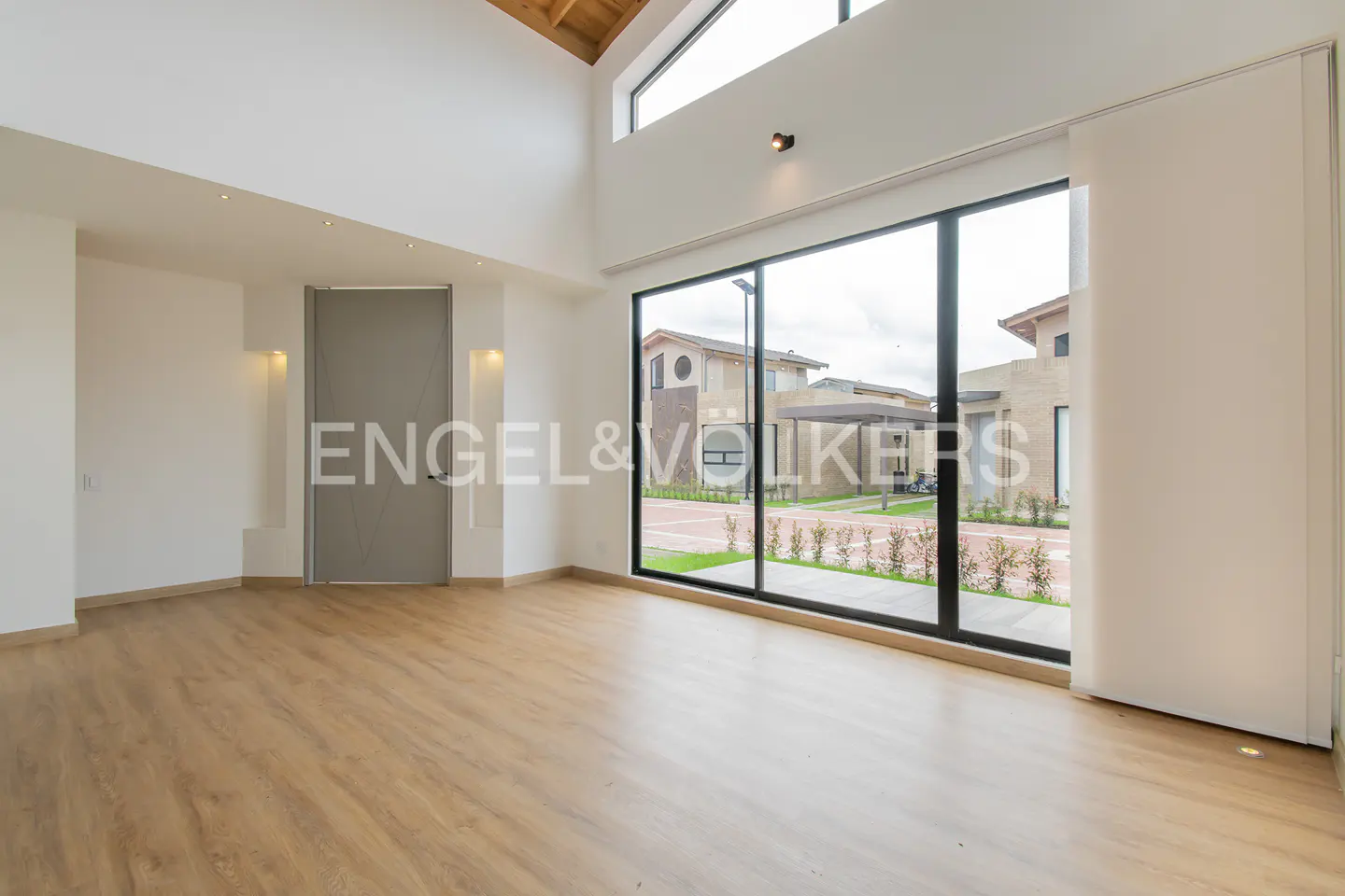 Bright, empty room with wood floors, white walls, and a large window showing a house outside.