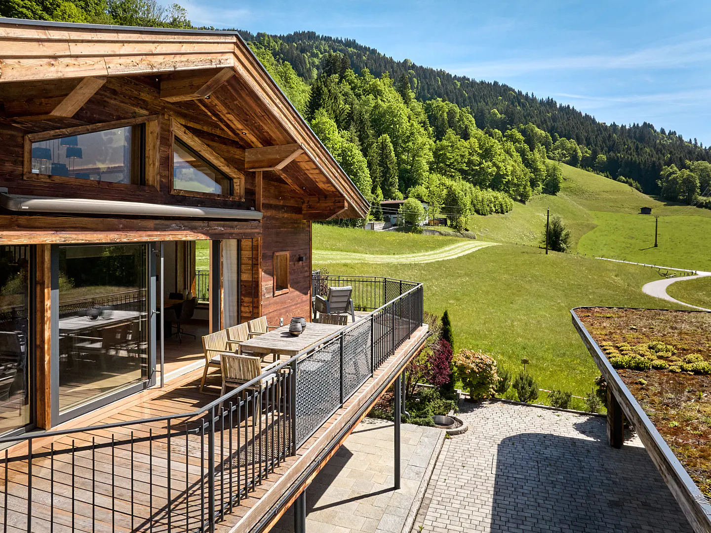 Exterior view of a wood cabin with a balcony overlooking a green meadow and forest.