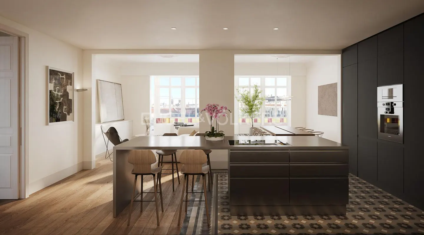 A modern kitchen with a gray island, wooden stools, and black cabinets. The floor has a patterned tile design. Large windows provide natural light.
