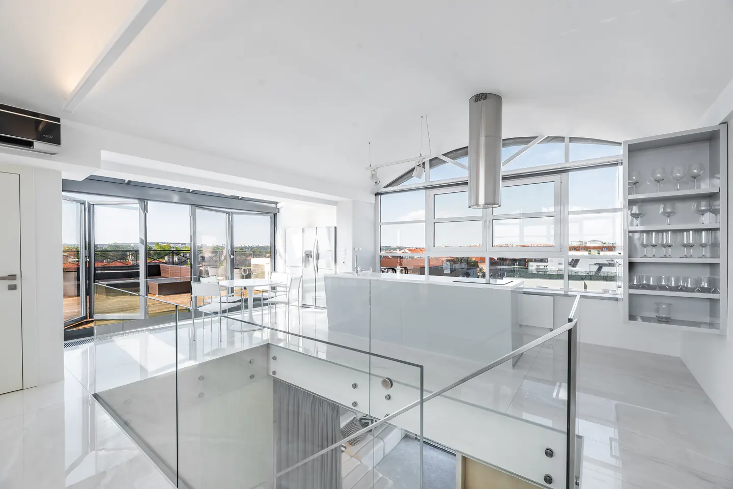 Bright, modern loft with white marble floors, glass railings, and a kitchen island. Large windows offer city views.