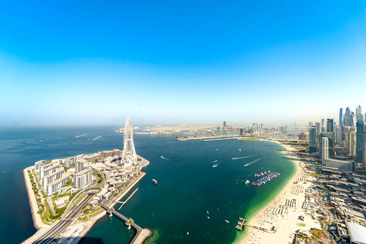 Aerial view of Dubai's coastline featuring the Ain Dubai Ferris wheel, beaches, and modern skyscrapers under a clear blue sky.