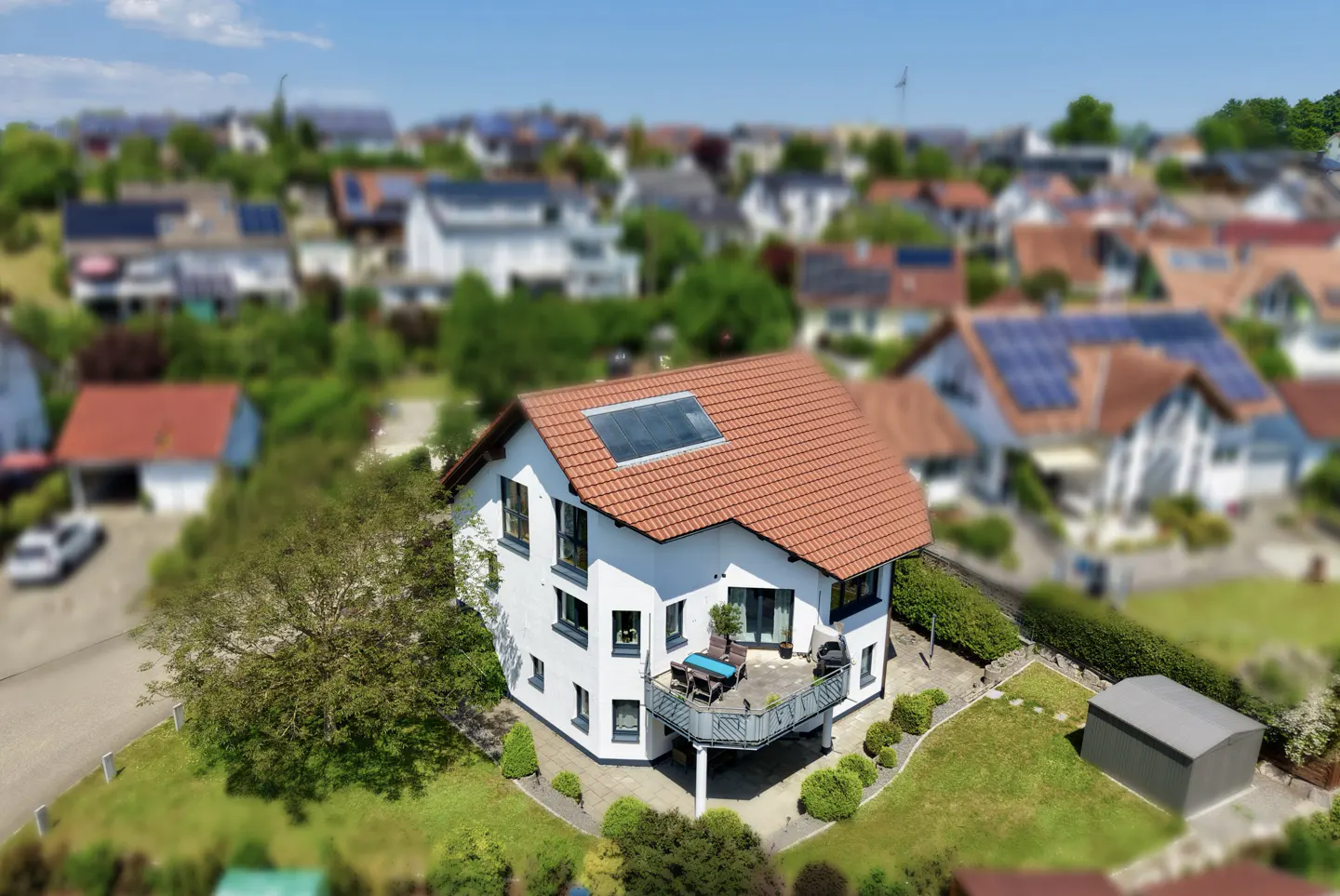 Aerial view of a white two-story house with a red tile roof, solar panels, and a balcony in a suburban neighborhood.