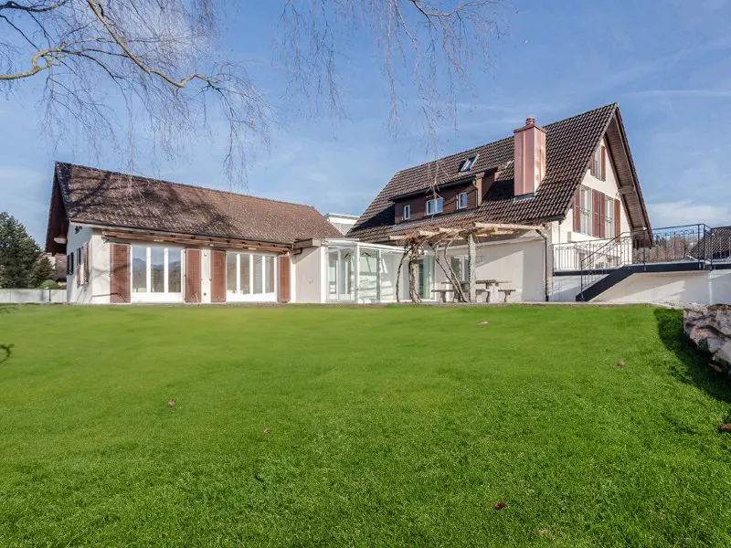 Exterior view of a white house with brown shutters and a large green lawn on a sunny day.