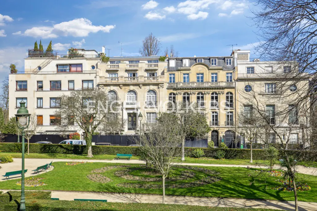 Row of elegant townhouses behind a green park with benches and trees under a blue sky.