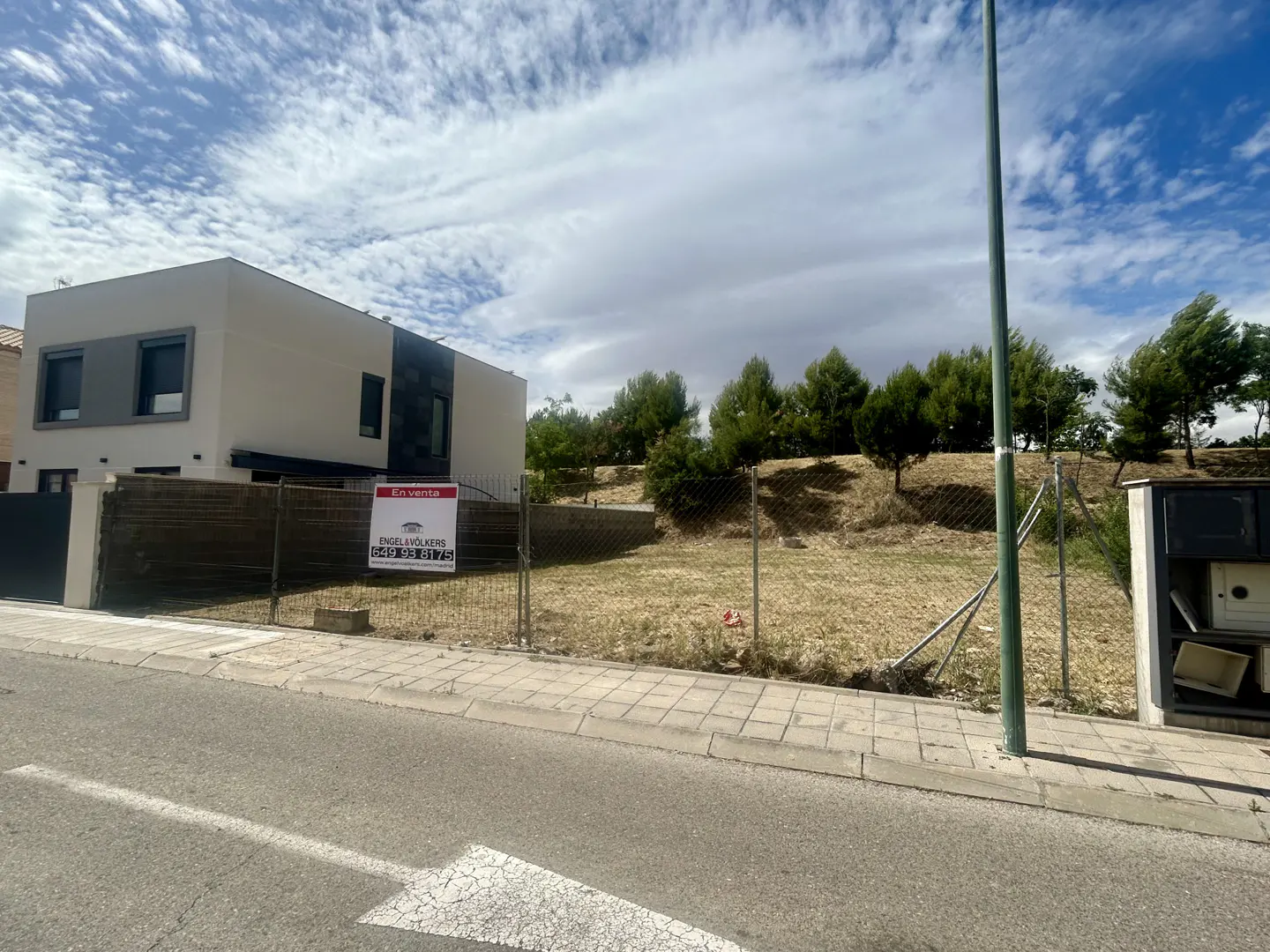 A vacant lot for sale next to a modern two-story house, featuring a chain-link fence and an Engel & Völkers sign.