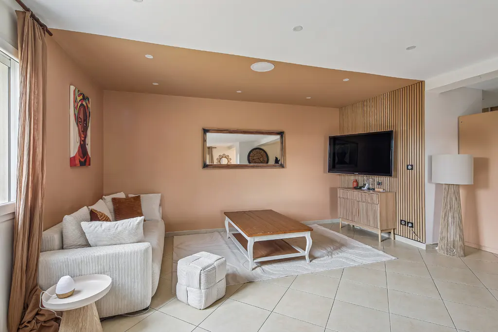 Living room with peach walls, a white sofa, a wooden coffee table on a white rug, and a TV on a wooden slat wall.
