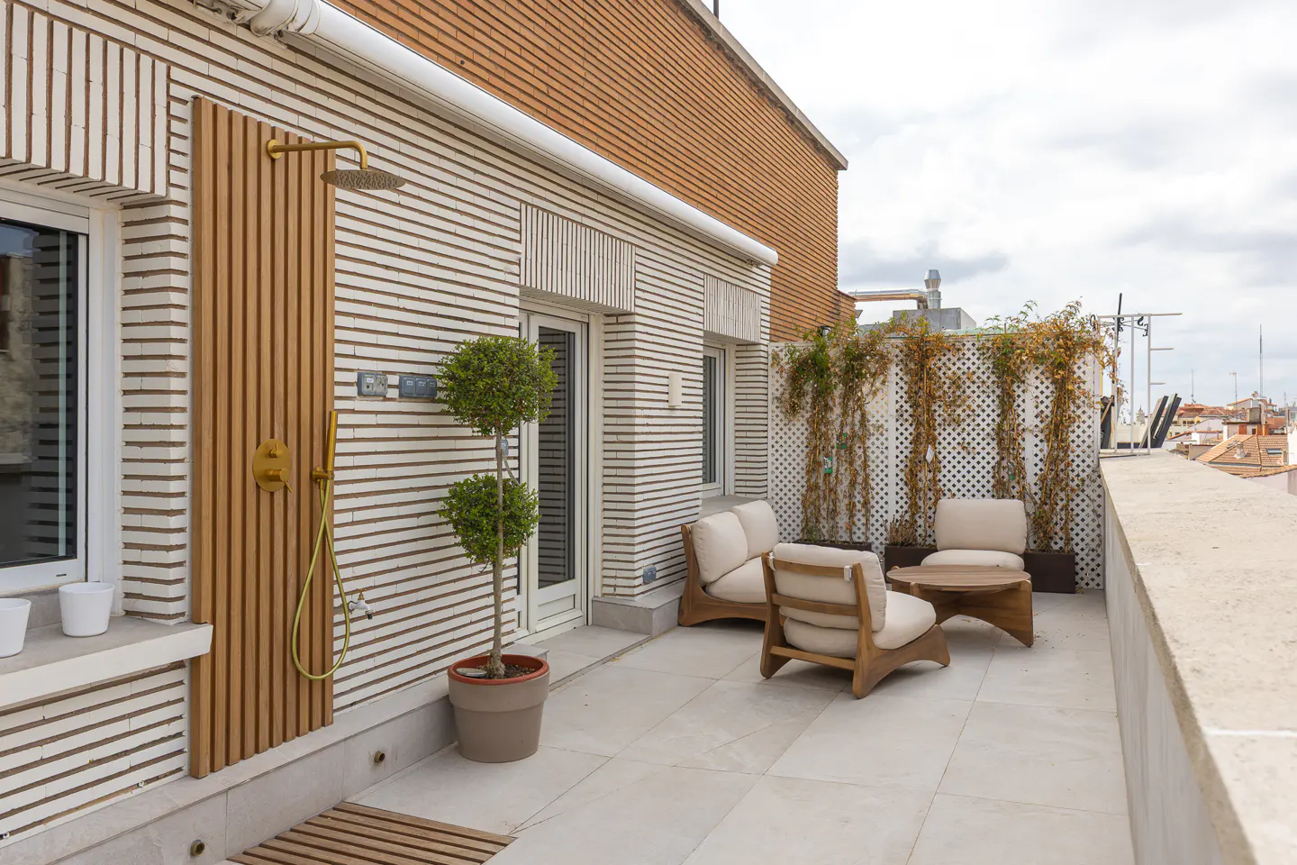 A rooftop patio with outdoor shower, seating, and a view of the city. The building has a unique horizontal brick pattern.