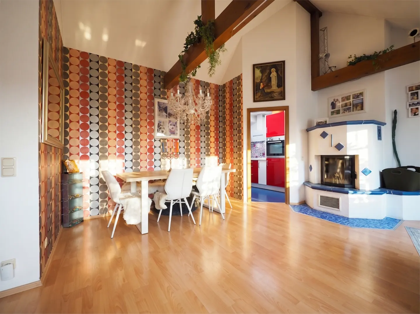 Bright dining room with wood floors, a table with white chairs, and a fireplace. A red kitchen is visible through a doorway.