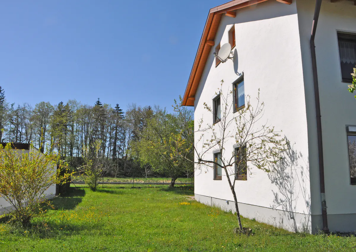 Side view of a white two-story house with brown trim, a satellite dish, and a green lawn.