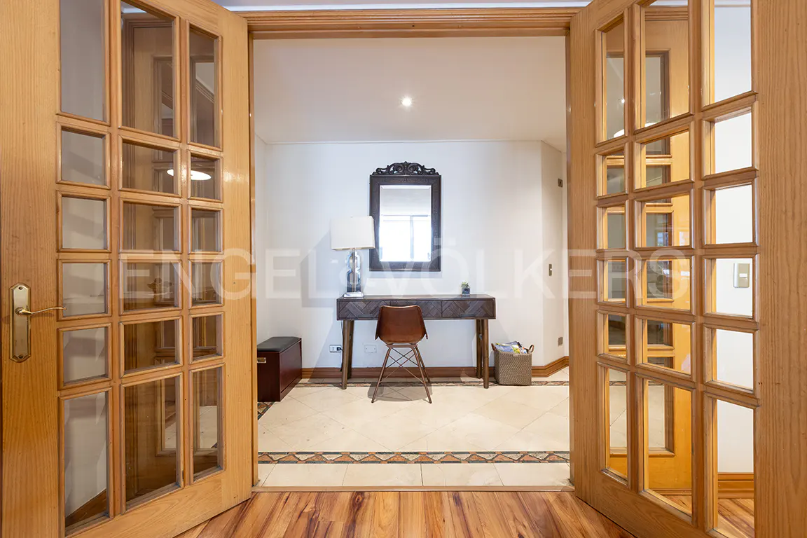 View through open wood-framed glass doors into a bright room with a desk, chair, lamp, and mirror.