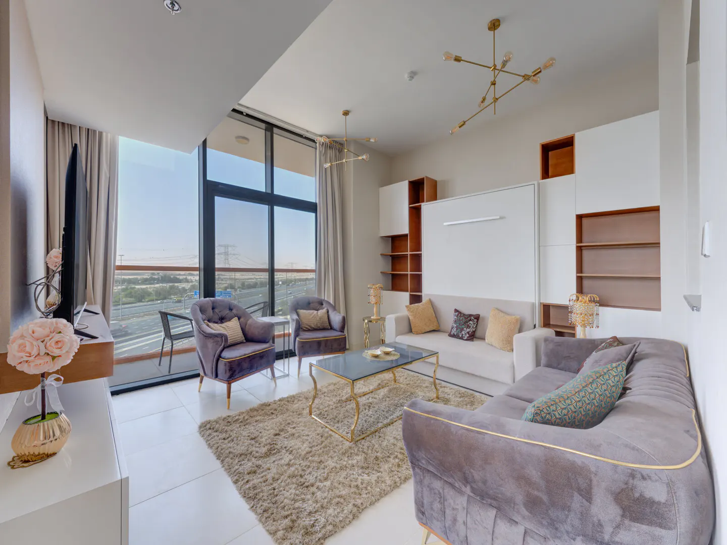 Bright living room with a gray sofa, two purple armchairs, and a glass coffee table on a beige rug. Large windows offer a city view.