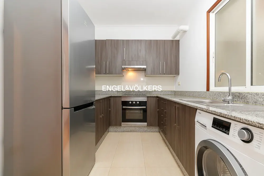 A modern kitchen with gray cabinets, granite countertops, stainless steel appliances, and a washing machine.