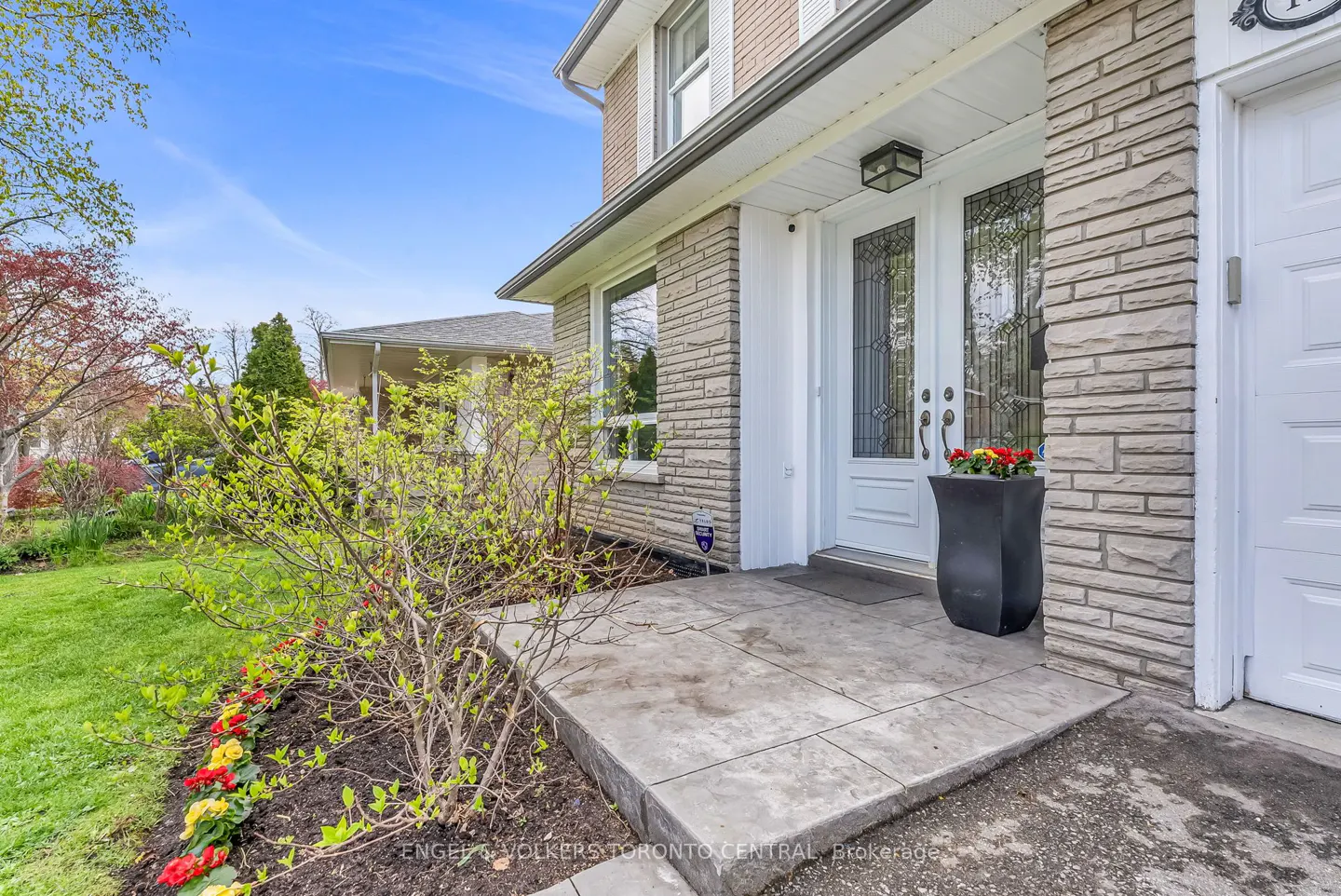 Exterior view of a two-story house with a white front door, stone facade, and flower bed.