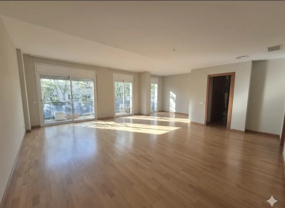 Bright, empty living room with light wood floors, white walls, and sliding glass doors to a balcony.
