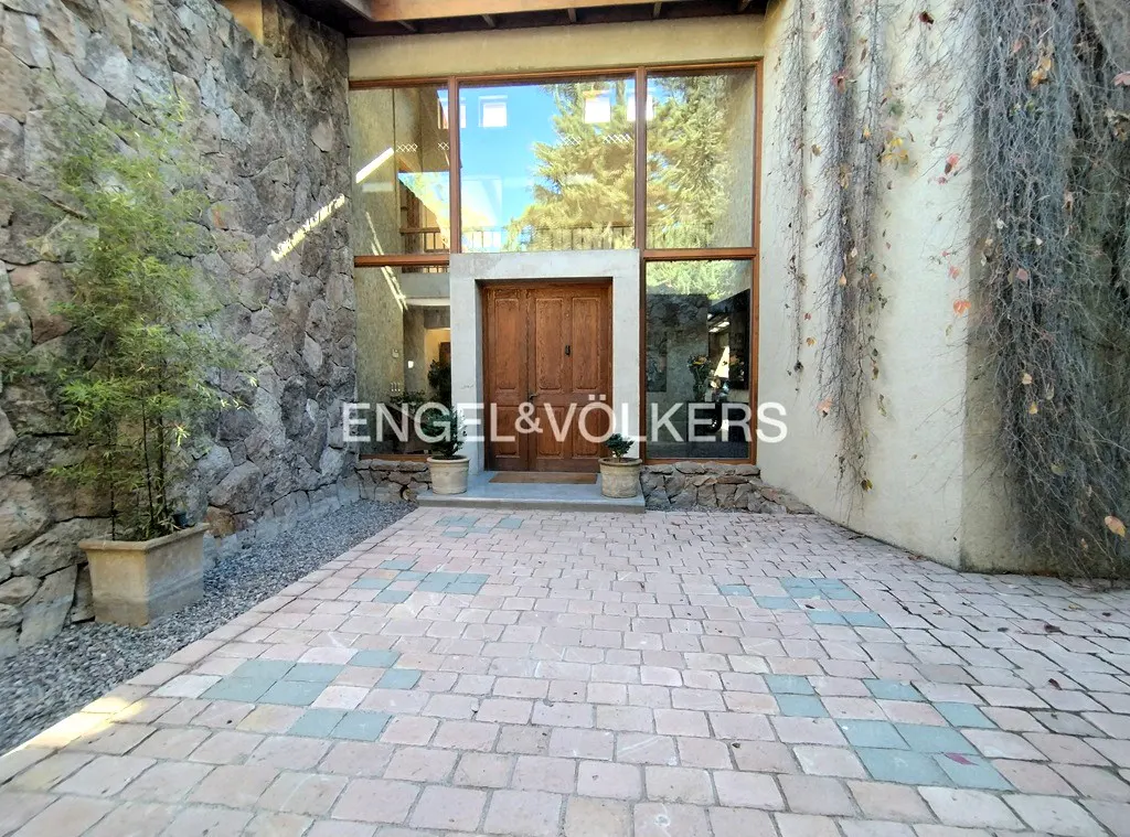 Stone facade with large windows and a wooden door. Vines climb the right wall. Paved walkway leads to the entrance.