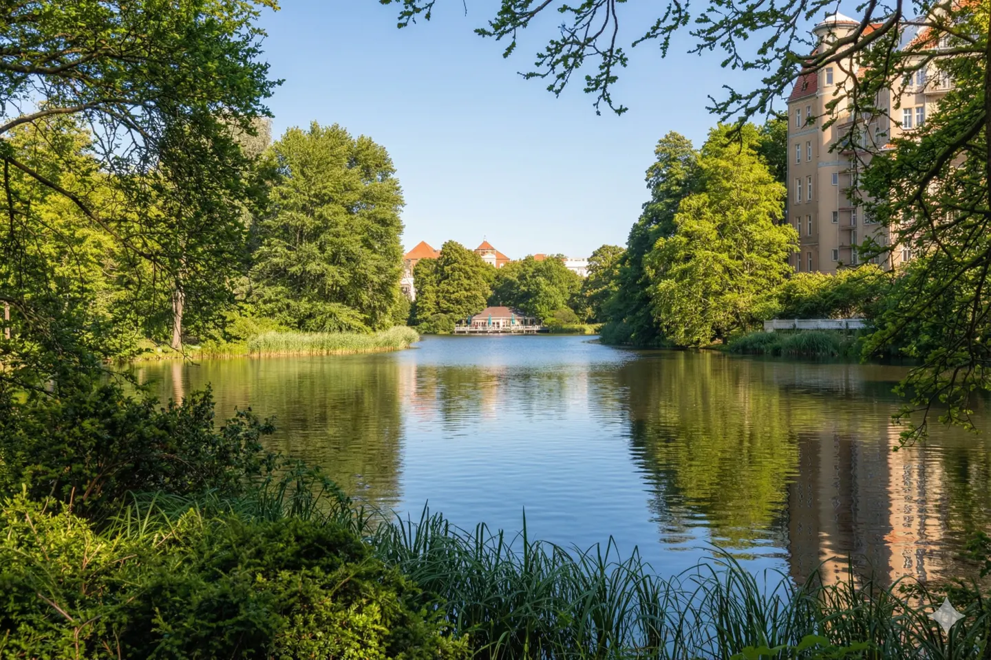 Scenic view of a calm lake surrounded by lush green trees and foliage, with buildings visible in the background.