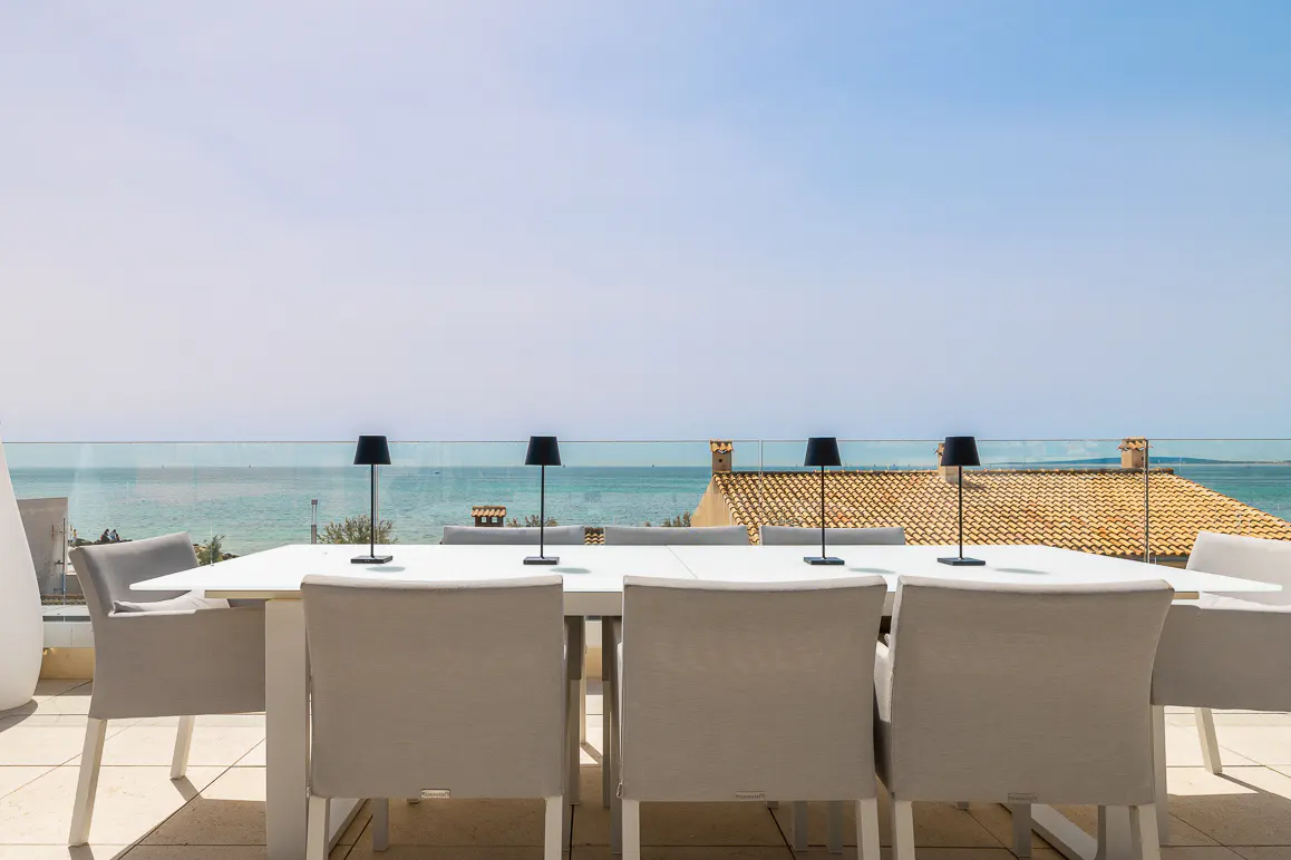 Outdoor dining area with a white table, gray chairs, and black lamps. Ocean view with a clear blue sky in the background.
